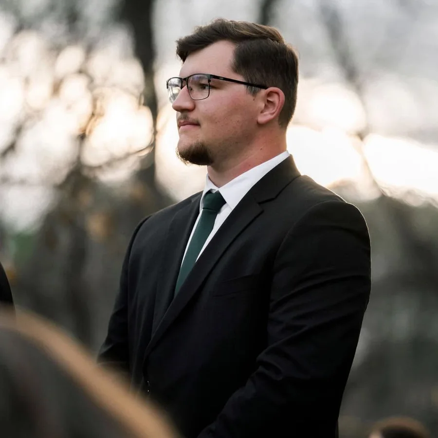 AJ Smalley, owner and DJ of Southern Goose Sound Co., in a black suit at an outdoor wedding